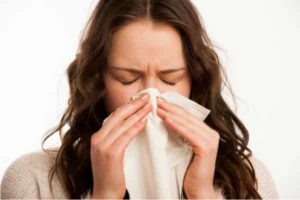 Woman with closed eyes holding a tissue to her nose, illustrating allergy symptoms related to poor air quality and dirty duct systems.