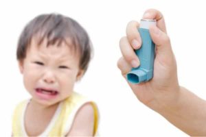 Child experiencing asthma symptoms with an inhaler, highlighting the importance of managing asthma and allergies related to air quality.