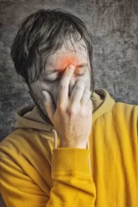 Man in a yellow hoodie holding his forehead, showing signs of discomfort, possibly related to sinus pain or headaches caused by respiratory issues from dirty air ducts.