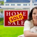 Woman smiling beside a "Home Sold" sign, representing successful home buying and HVAC considerations for new homeowners in Montgomery.