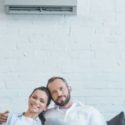 Couple relaxing indoors with a wall-mounted air conditioning unit, highlighting the importance of HVAC systems for home comfort.