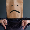 Person with a paper bag over their head, sad face, and thumbs-down gesture, indicating HVAC service disappointment.