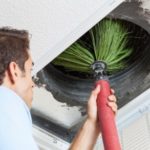 Person cleaning an air duct indoors with a bristle tool for HVAC maintenance at Chad's AC Direct.