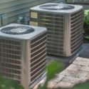Two air conditioning units on stone surface, surrounded by green foliage, highlighting Chad's AC Direct HVAC solutions.
