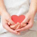 Two hands gently cupping a red heart cutout, symbolizing care and compassion, relevant to HVAC services by Chad's AC Direct.