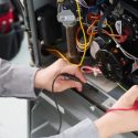 Technician's hands repairing HVAC electrical components with wires and a multimeter at Chad's AC Direct.