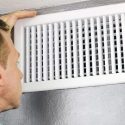 Person inspecting an air vent at home, showing the white slatted design, related to Chad's HVAC services for comfort.
