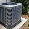 Gray air conditioning unit on concrete pad with fan, showcasing HVAC solutions from Chad's AC Direct.
