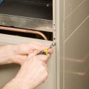 Person repairing HVAC components with a screwdriver in a metallic cabinet, showcasing manual skill at Chad's AC Direct.