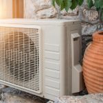 Air conditioner unit next to a decorative pot on a stone wall with greenery, highlighting HVAC in an outdoor setting.