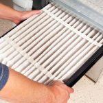 Person holding a dirty air filter for HVAC maintenance at Chad's AC Direct, emphasizing the importance of clean air systems.
