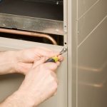 Hands using a screwdriver on a metal panel during HVAC maintenance at Chad's AC Direct.