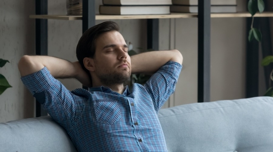 Man relaxing on a couch with hands behind his head, representing comfort and peace of mind in a clean air environment.