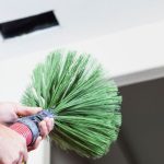 Person using a green duster to clean air ducts, emphasizing the importance of duct cleaning for better indoor air quality and HVAC maintenance.