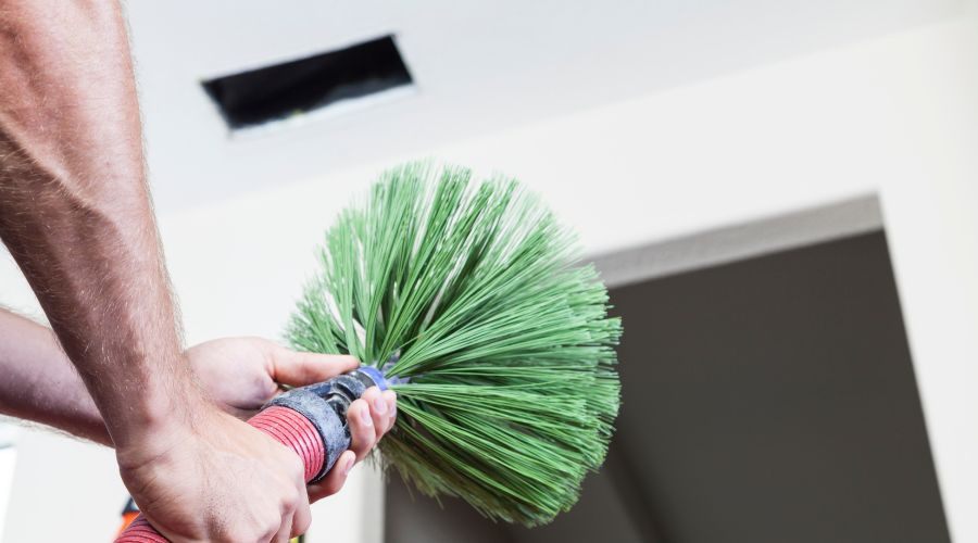 Person using a duct cleaning brush to clean air ducts, highlighting the importance of air duct maintenance for indoor air quality and HVAC efficiency.