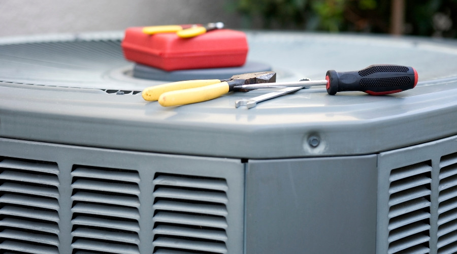Tools on top of an air conditioning unit, including pliers, screwdrivers, and a red toolbox, representing AC repair services.